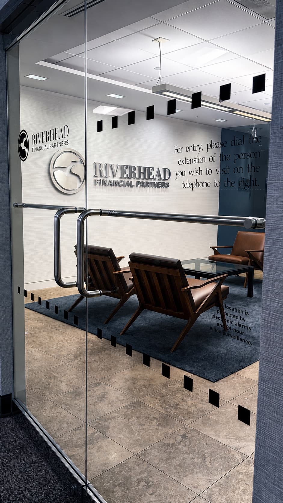 Glass entry doors to the Riverhead Financial Partners suite, with the firm's name on the reception wall and leather chairs in the waiting area.